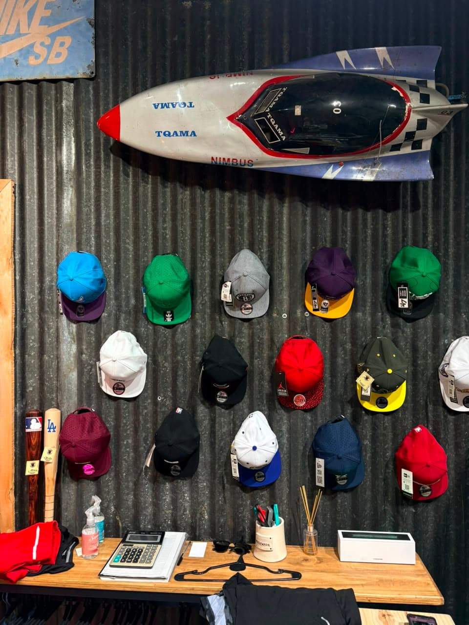 Pared de chapa con quince gorras de béisbol colgadas y bates apoyados al costado